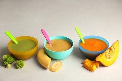 Bowls with different baby food on gray background