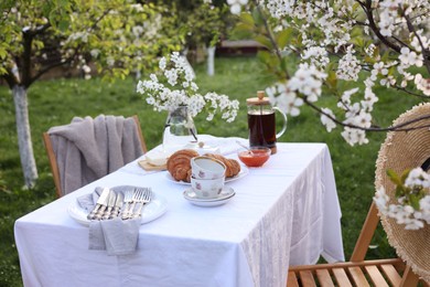 Photo of Stylish table setting with beautiful spring flowers, tea and croissants in garden