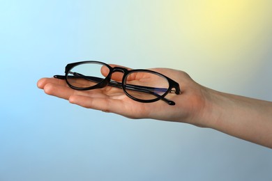Photo of Woman holding glasses with black frame on color background, closeup