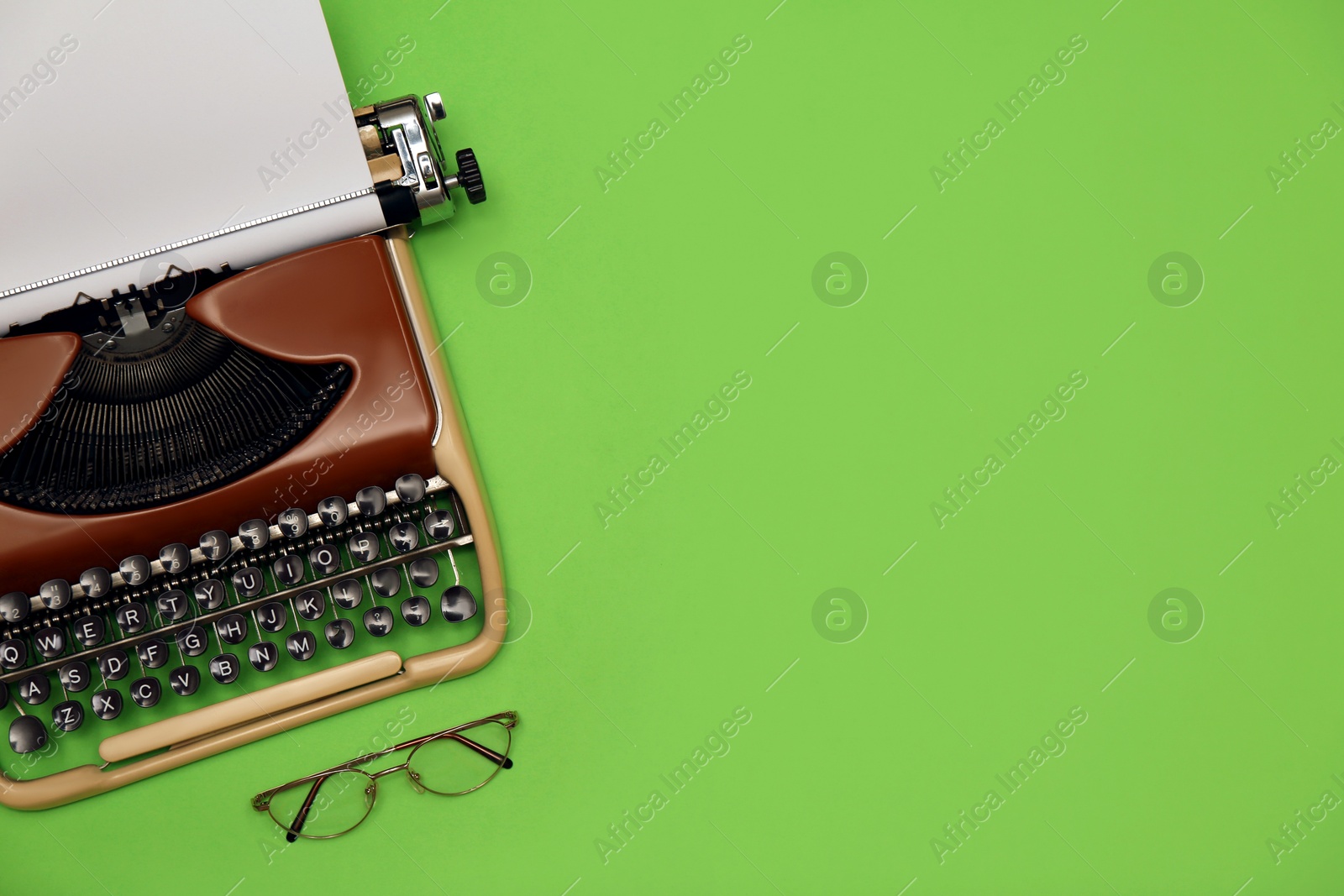 Photo of Vintage typewriter with sheet of paper and glasses on green background, flat lay. Space for text