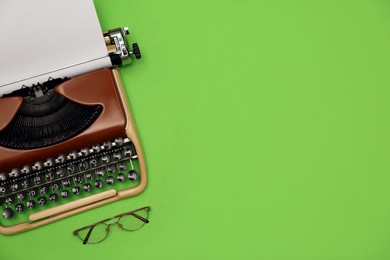 Vintage typewriter with sheet of paper and glasses on green background, flat lay. Space for text