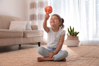 Little girl enjoying air flow from portable fan on floor in living room. Summer heat