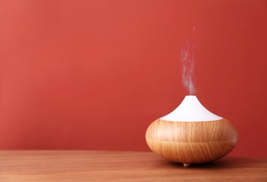 Photo of Essential oils diffuser on wooden table near red wall. Space for text