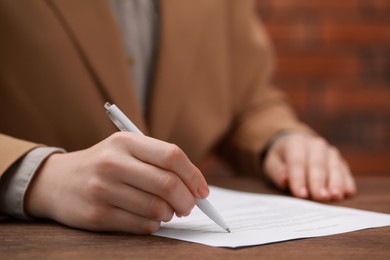 Woman signing documents at wooden table in office, closeup. Space for text