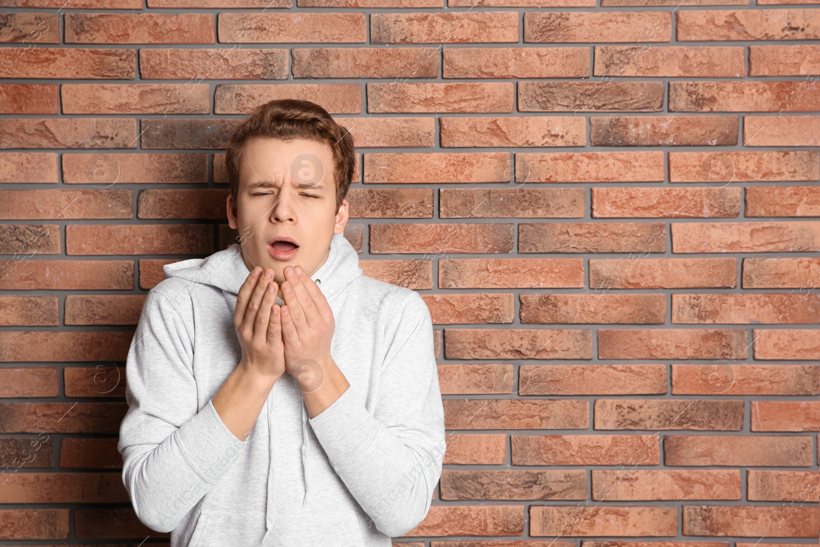 Photo of Teenage boy suffering from cough near brick wall. Space for text