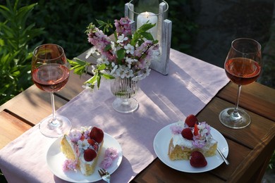 Photo of Vase with spring flowers, wine and cake on table served for romantic date in garden