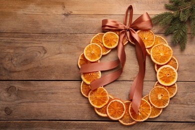 Decorative wreath made with dry oranges, ribbon and fir branch on wooden table, flat lay. Space for text