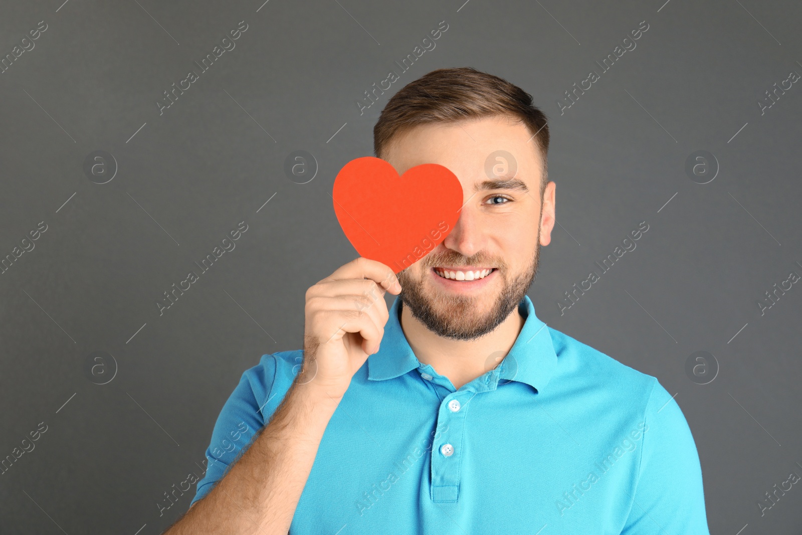 Photo of Young man with paper heart on grey background. Space for text