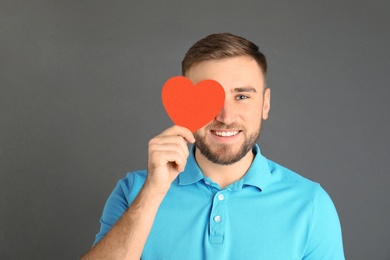 Photo of Young man with paper heart on grey background. Space for text
