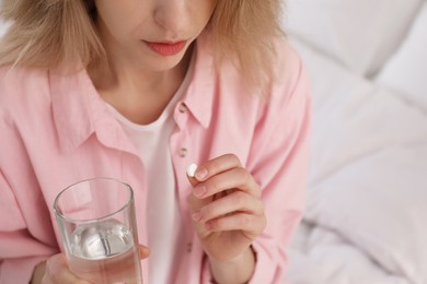 Photo of Young woman with abortion pill and glass of water on bed, closeup