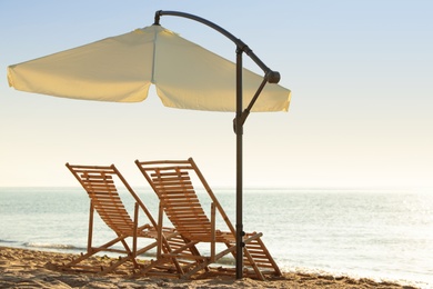 Photo of Wooden deck chairs and outdoor umbrella on sandy beach. Summer vacation