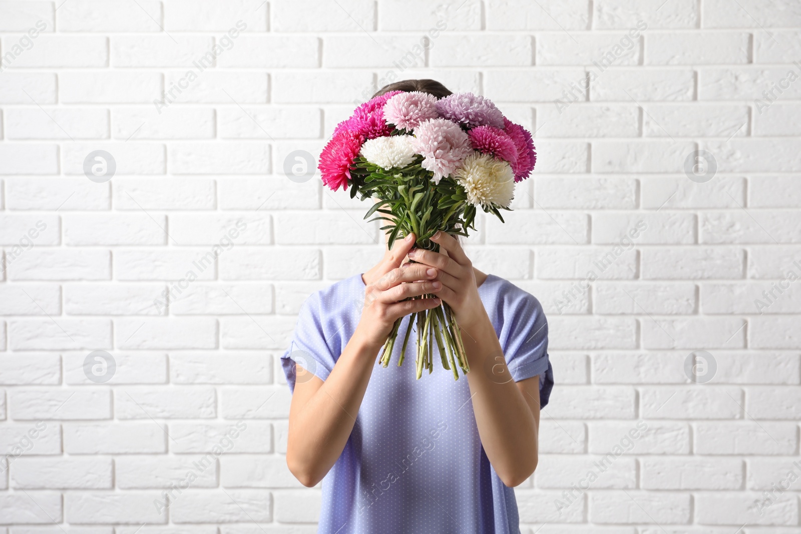 Photo of Woman holding beautiful aster flower bouquet against brick wall