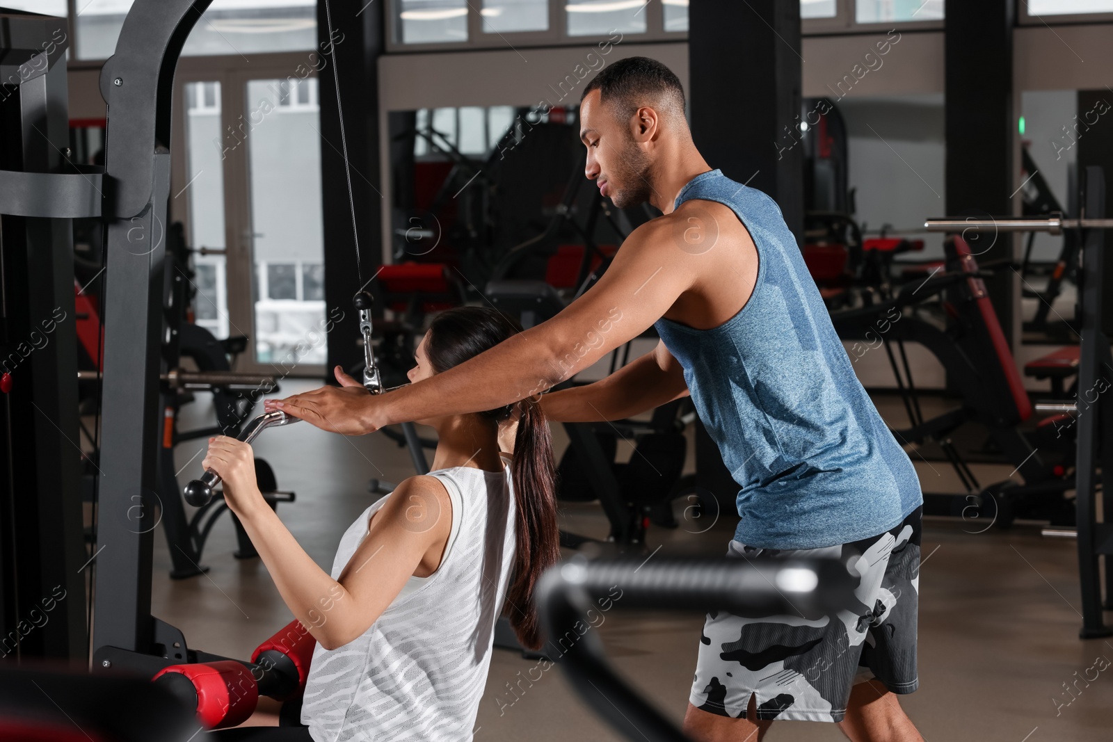 Photo of Young woman working out with professional trainer in modern gym