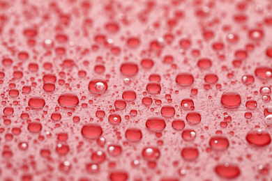 Photo of Water drops on red background, closeup view