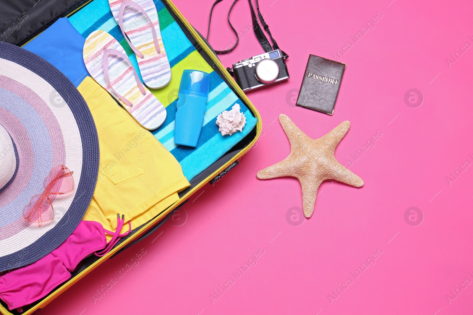 Photo of Open suitcase and beach objects on pink background, flat lay