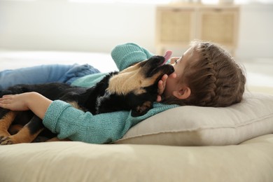 Photo of Little girl with cute puppy lying on soft pillow at home