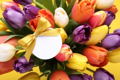Photo of Bouquet of beautiful colorful tulips with blank card on yellow background, closeup. Birthday celebration