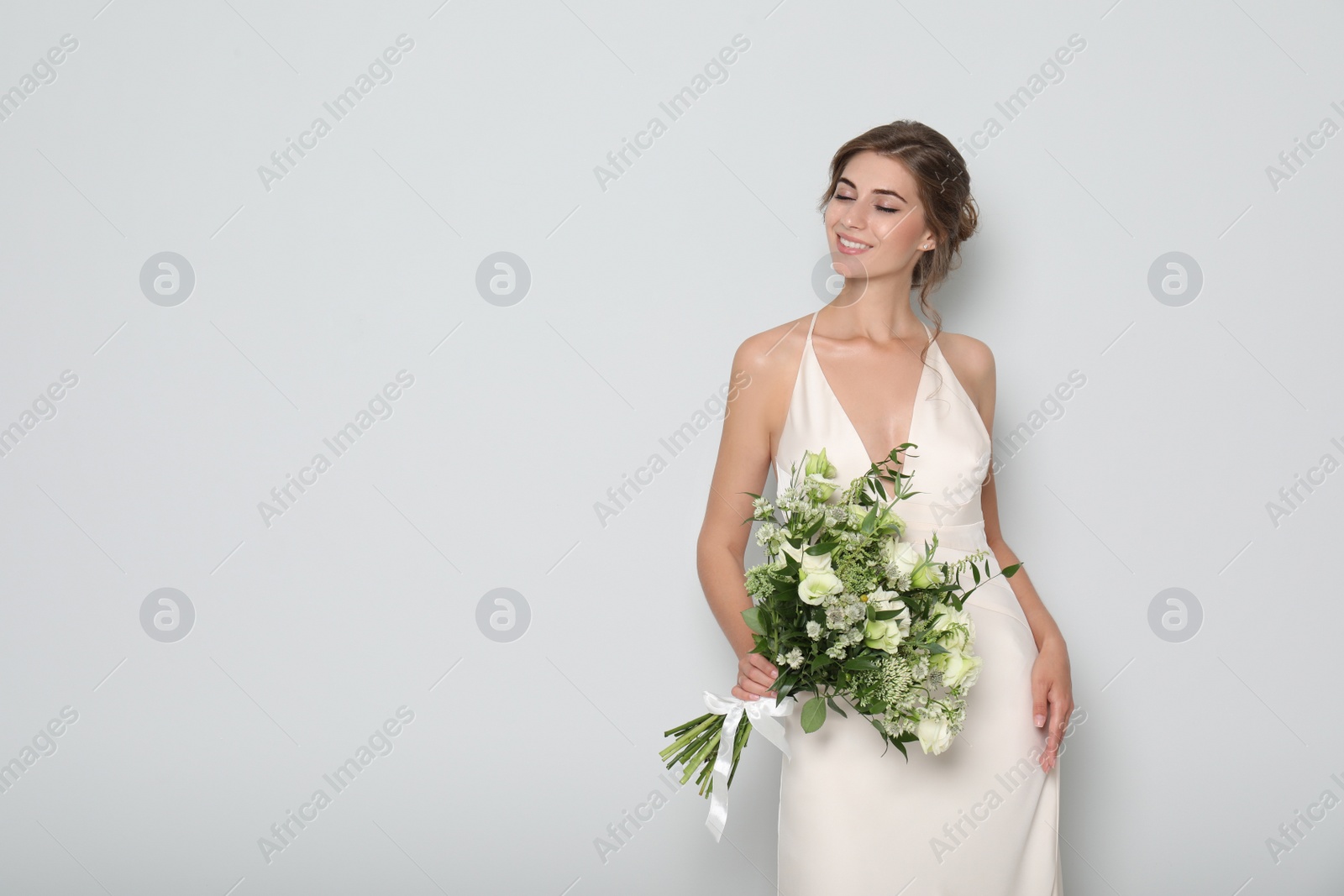 Photo of Young bride wearing wedding dress with beautiful bouquet on light grey background. Space for text