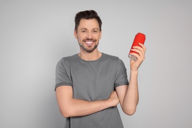 Happy man holding red tin can with beverage on light grey background