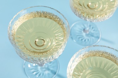 Photo of Glasses of expensive white wine on light blue background, above view
