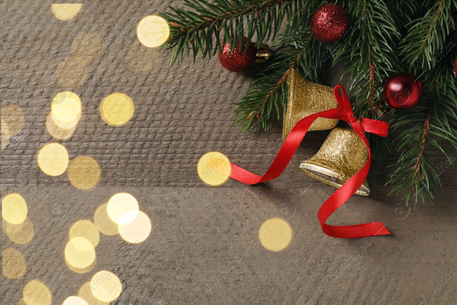 Photo of Christmas bells and fir tree branches with festive decor on wooden table, flat lay. Space for text