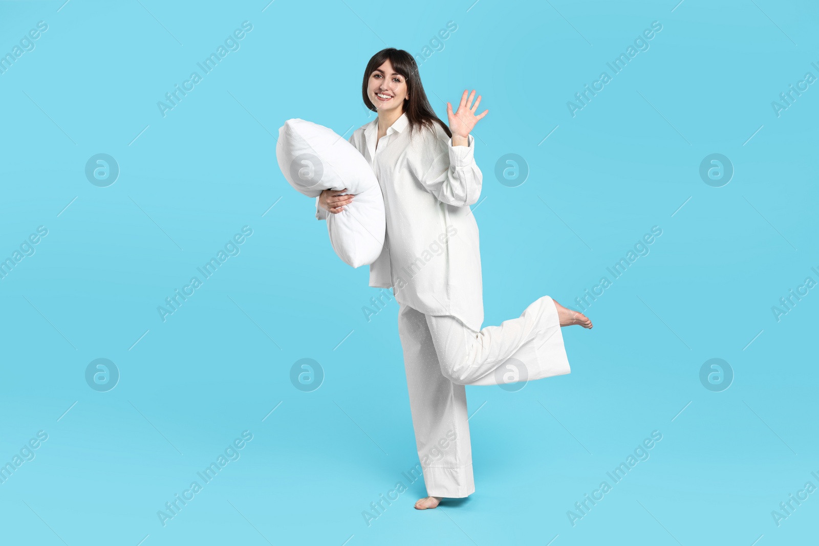 Photo of Happy woman in pyjama holding pillow on light blue background