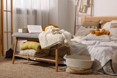Photo of Large comfortable bed with soft sweaters, pillows and blanket in room. Home textile