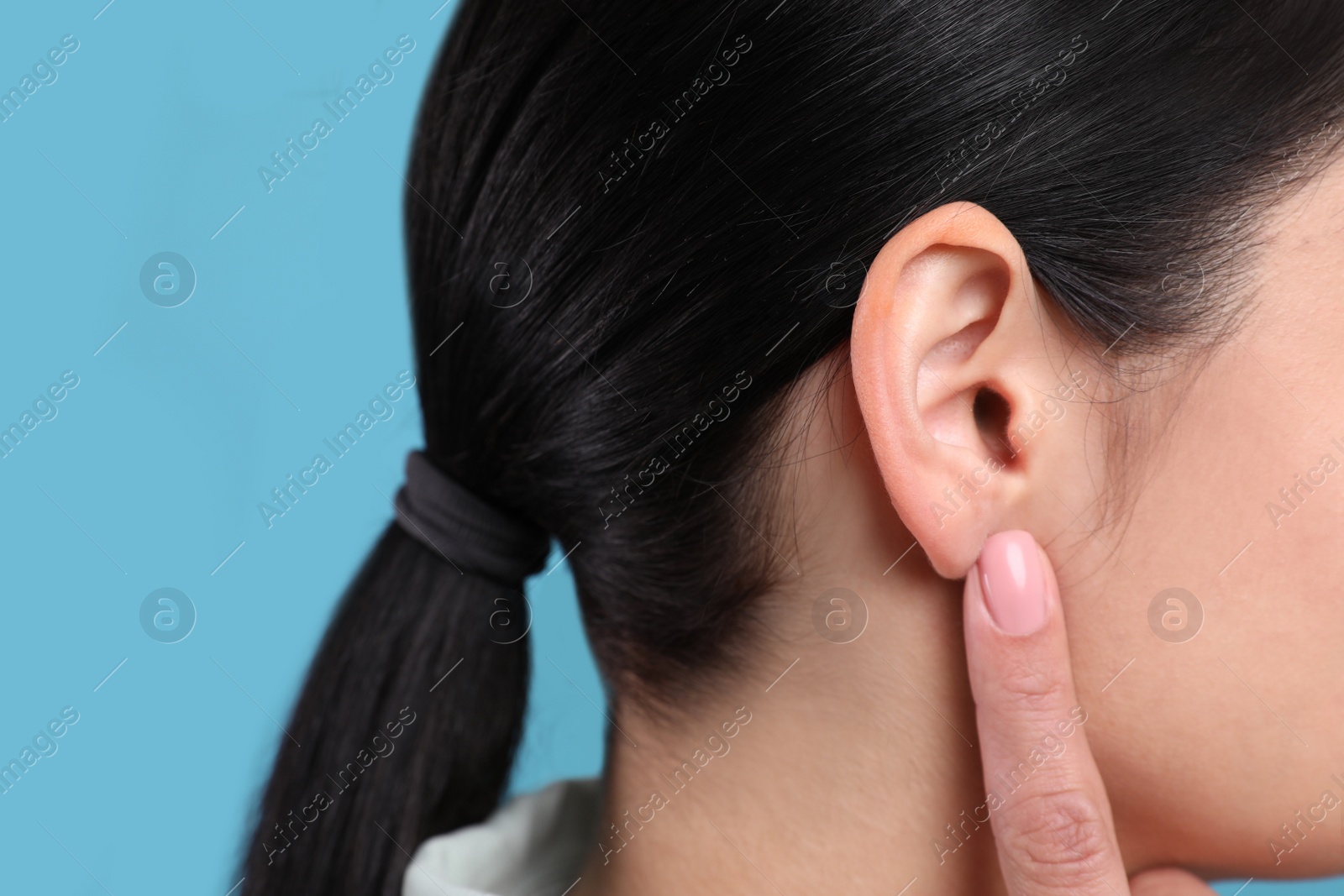 Photo of Woman pointing at her ear on light blue background, closeup