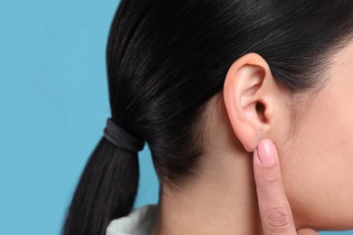 Photo of Woman pointing at her ear on light blue background, closeup