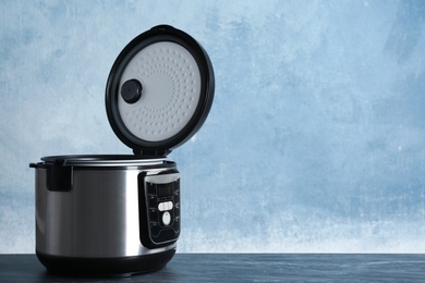 Photo of Modern powerful multi cooker on table against color background. Space for text
