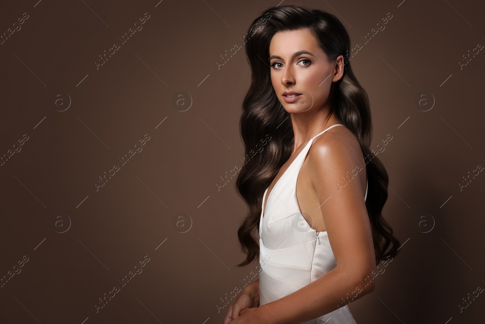Image of Gorgeous woman with shiny wavy hair on brown background, space for text. Professional hairstyling