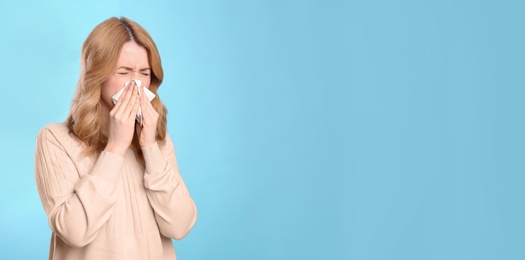 Woman with tissue suffering from runny nose on light blue background. Space for text