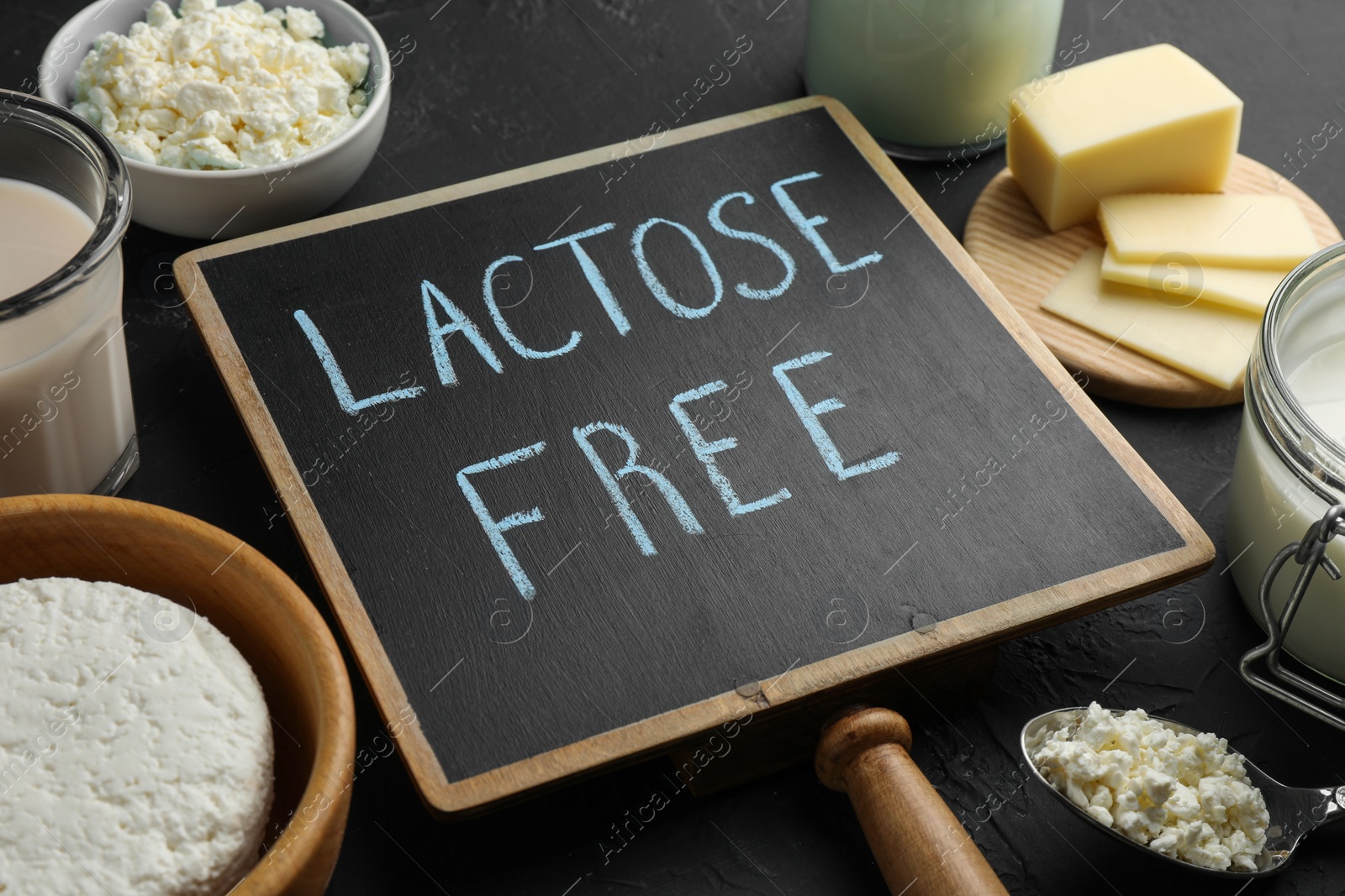 Photo of Dairy products and board with phrase Lactose free on black textured table