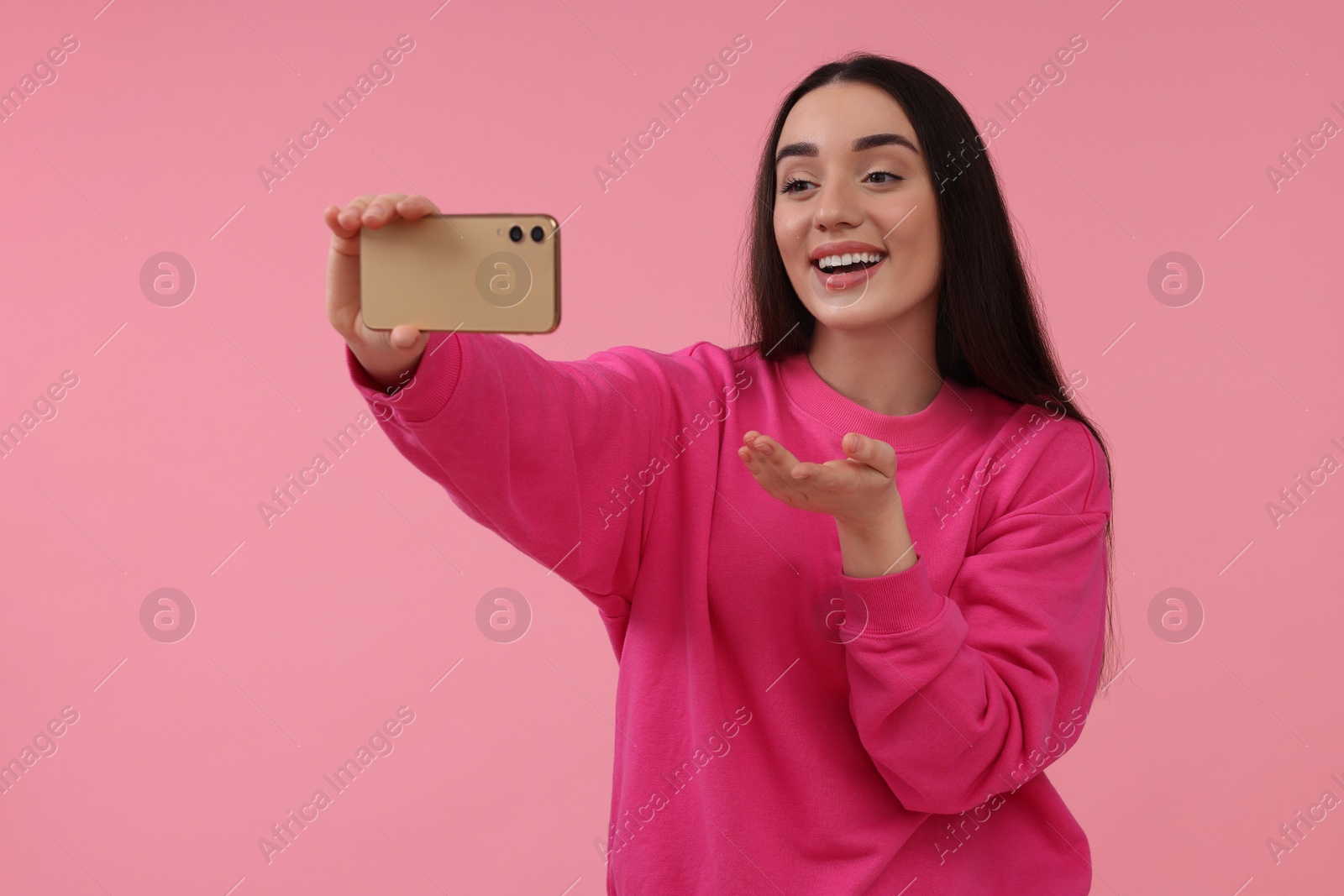 Photo of Smiling young woman taking selfie with smartphone on pink background, space for text