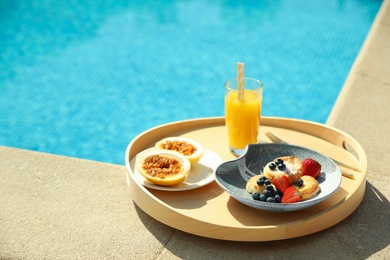 Photo of Tray with delicious breakfast near swimming pool