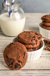 Photo of Bowl with tasty chocolate chip cookies on wooden table