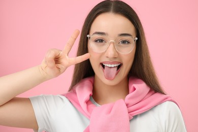 Photo of Happy woman showing her tongue and V-sign on pink background