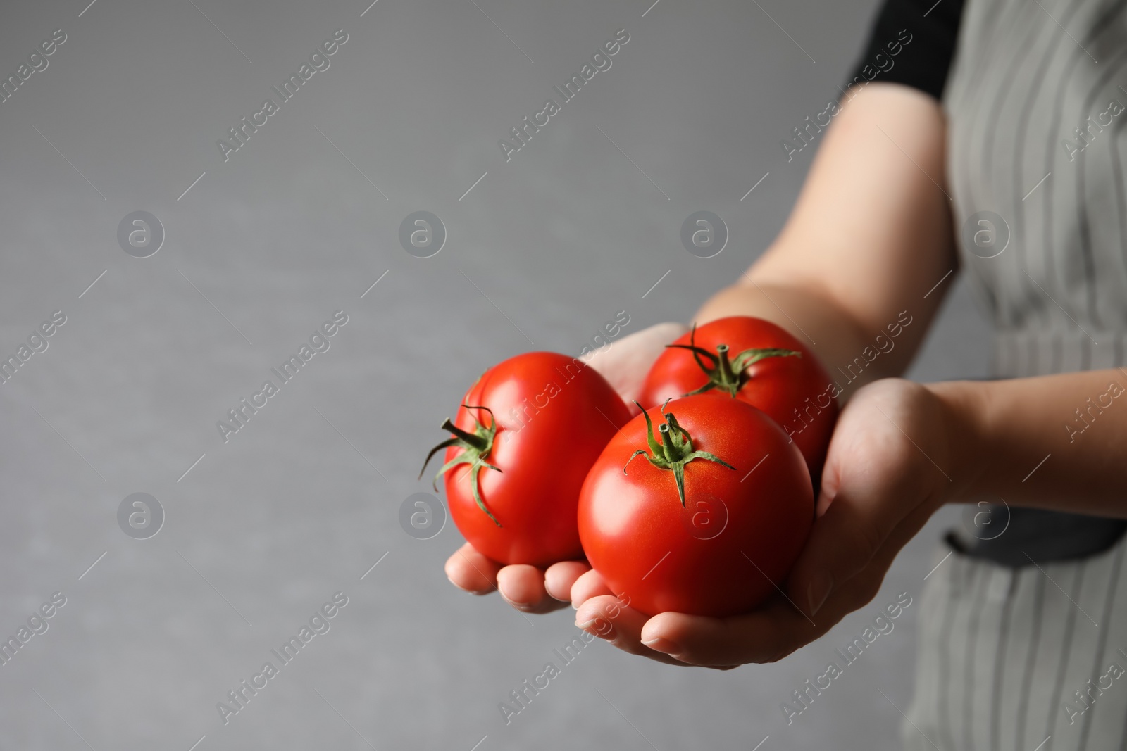 Photo of Woman with ripe tomatoes on grey background, closeup. Space for text