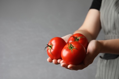 Photo of Woman with ripe tomatoes on grey background, closeup. Space for text