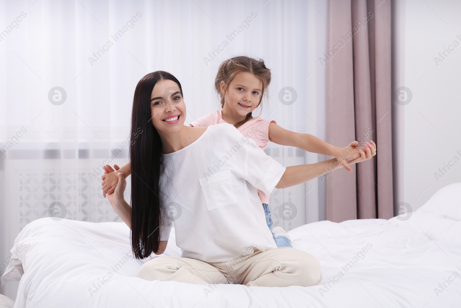 Photo of Happy woman and her daughter having fun on bed at home. Mother's day celebration