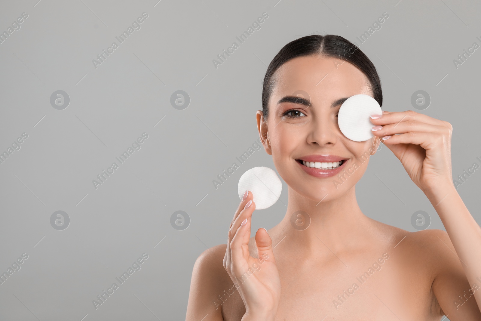 Photo of Beautiful woman removing makeup with cotton pads on light grey background, space for text