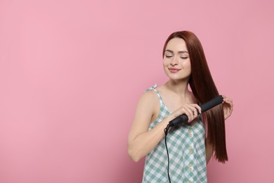 Beautiful woman using hair iron on pink background, space for text