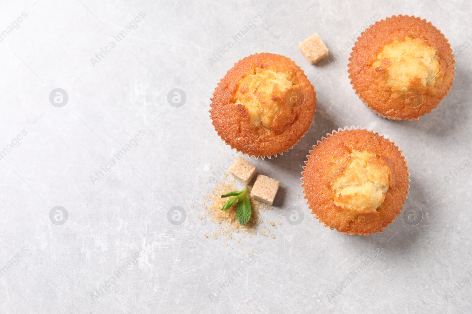 Photo of Delicious sweet muffins and brown sugar on light grey textured table, flat lay. Space for text