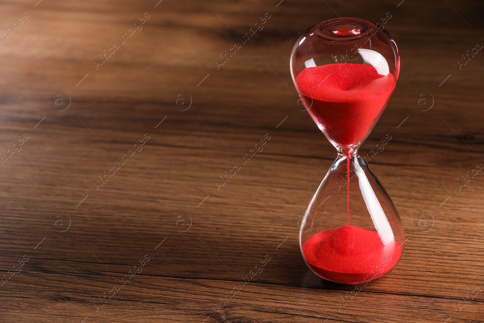 Photo of Hourglass with red flowing sand on wooden table. Space for text