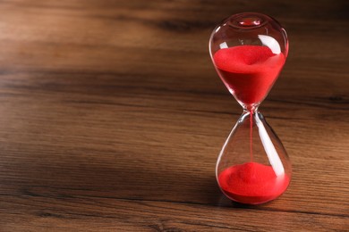 Photo of Hourglass with red flowing sand on wooden table. Space for text