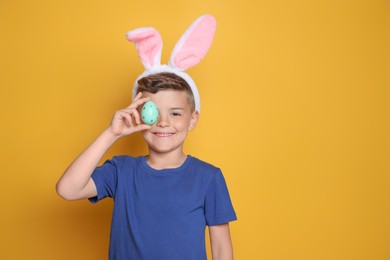 Photo of Cute little boy in bunny ears holding Easter egg on yellow background. Space for text