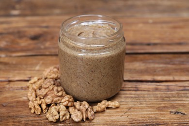 Photo of Tasty nut paste in jar and walnuts on wooden table, closeup