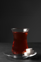 Photo of Glass with traditional Turkish tea and sugar cubes on black table