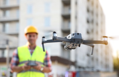 Builder operating drone with remote control at construction site, focus on quadcopter. Aerial survey