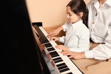 Young woman with child playing piano indoors. Music lesson